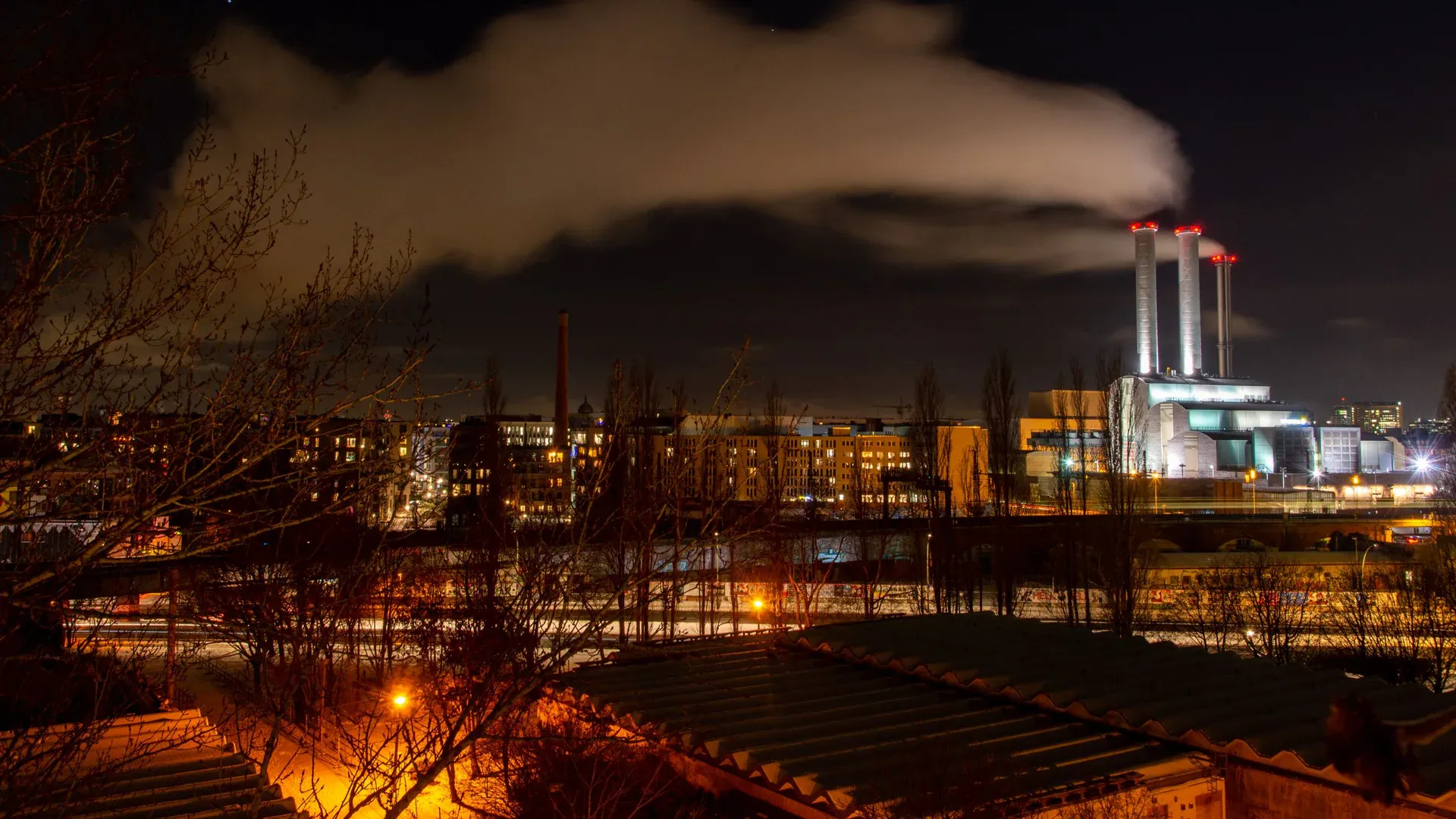 A vibrant city at night featuring an industrial power plant emitting smoke under a starry sky