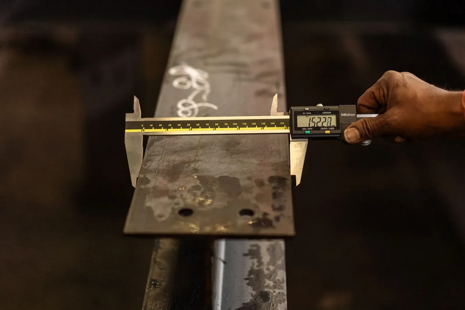 Worker using a digital caliper to measure the width of a metal beam
