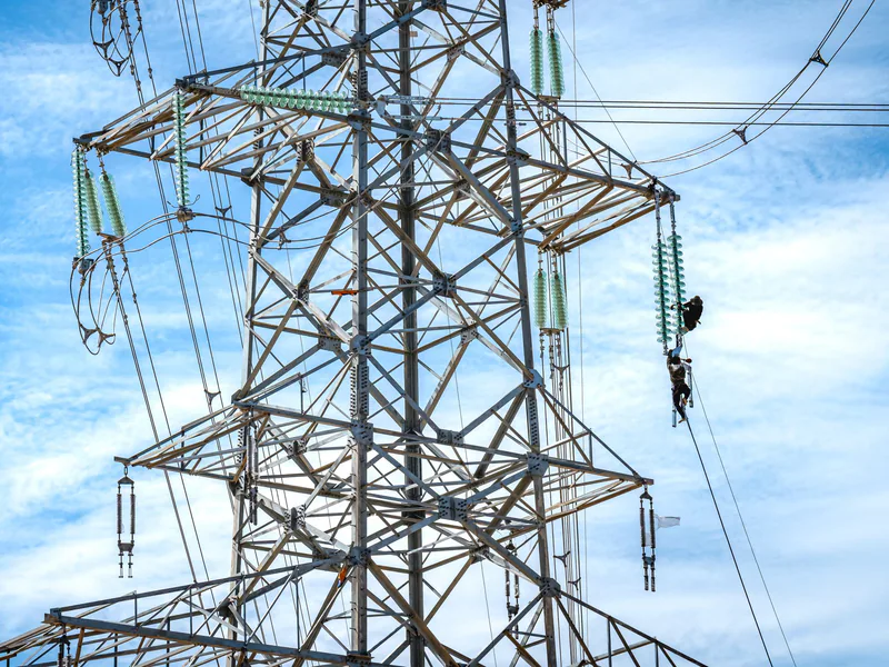 Workers performing maintenance on a high voltage power line against a blue sky