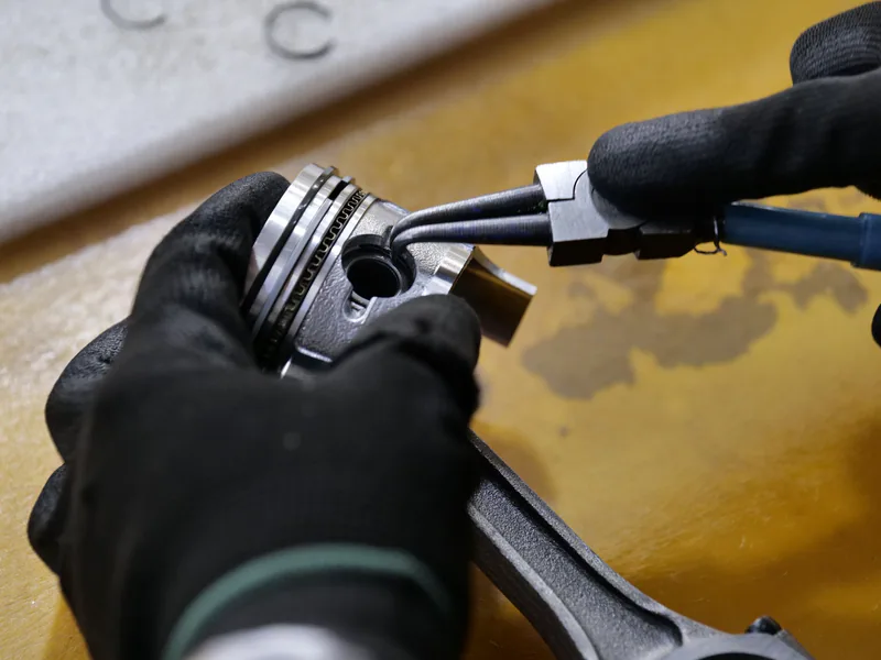 Gloved hands working on a piston rod in a workshop setting. Industrial repair scene