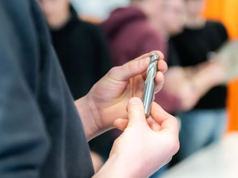 Hands carefully examining a metal drill bit during a workshop session