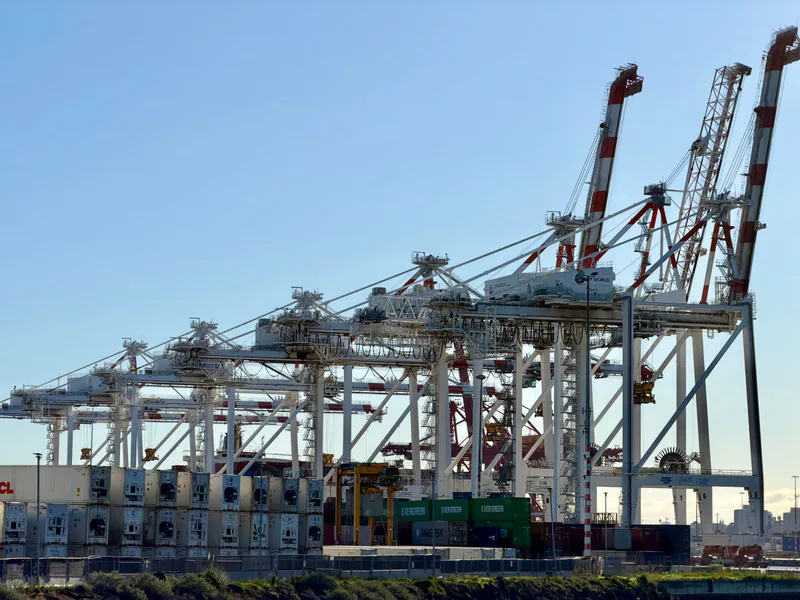 A view of shipping containers and cranes at a bustling port in Australia under clear skies