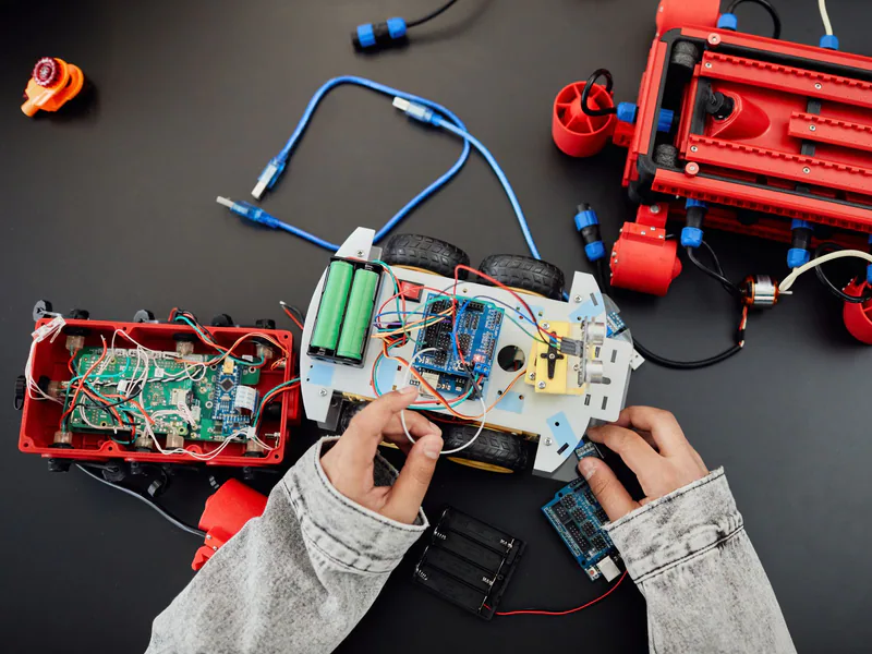 Young hands working on a robotics project with toy cars and circuits, focusing on innovation and education