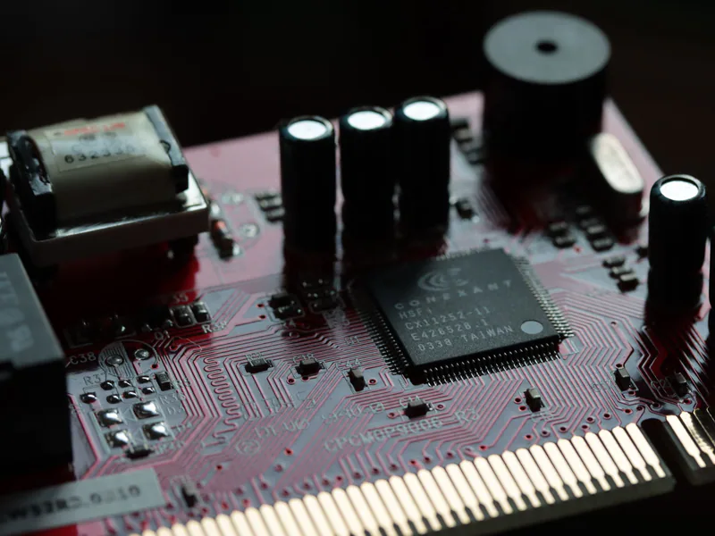 Detailed view of a red circuit board with various electronic components and microchip