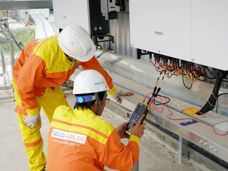 Two electrical engineers installing and testing solar power systems wearing safety gear at a construction site