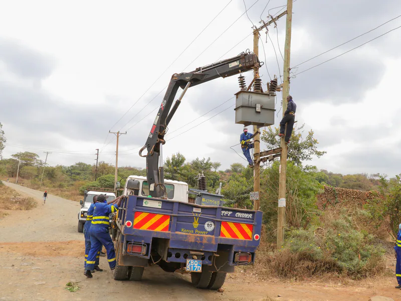Utility workers in protective gear servicing power lines with a truck crane on a rural road
