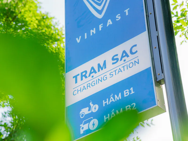 Close-up of a VinFast charging station sign with green leaves in the foreground, indicating eco-friendly technology