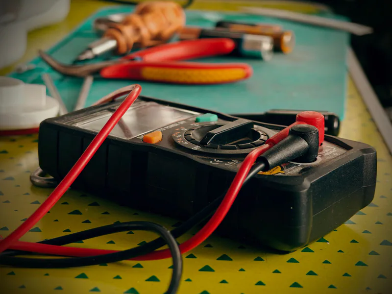 Close-up view of a multimeter and various tools on a workspace table