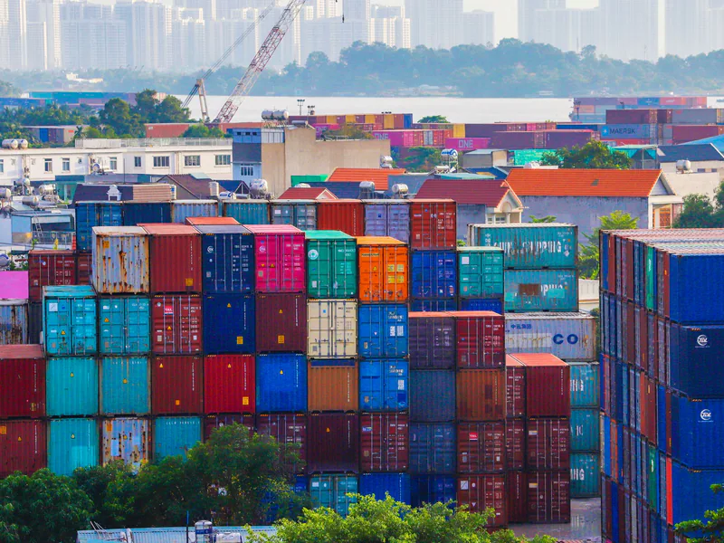 Vibrant stacked cargo containers at a bustling port with urban skyline in background