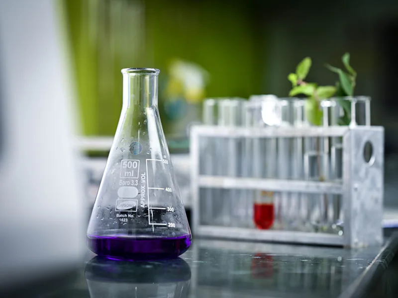 Close-up of a lab flask with purple liquid and test tubes in a scientific setting