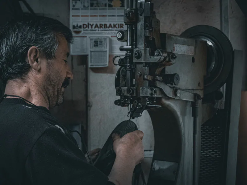 Skilled craftsman works with industrial sewing machine in workshop setting. Atmospheric and moody lighting