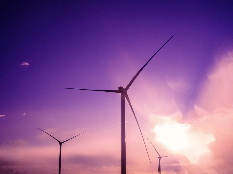 Three wind turbines silhouetted against a purple sunset sky, embodying renewable energy