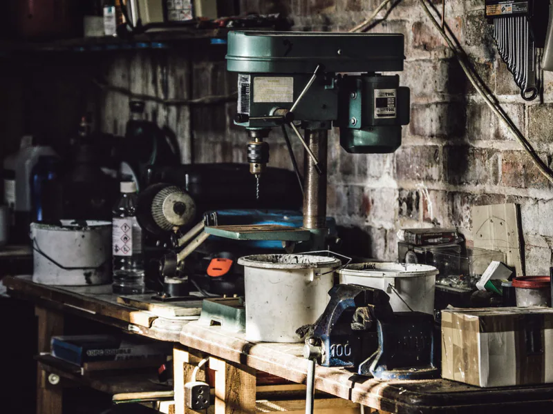 A detailed view of a cluttered workshop with a focus on a drill press and various tools