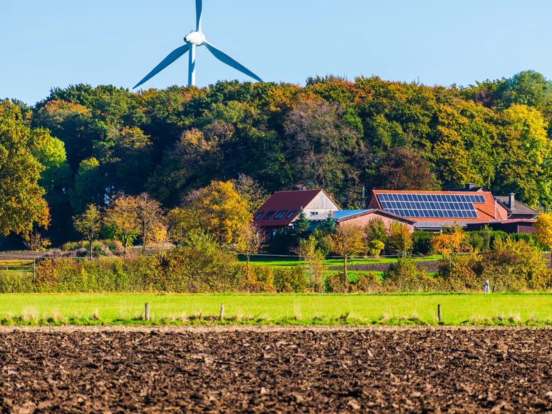 A picturesque sustainable farm featuring wind turbine and solar panels surrounded by vibrant autumn foliage