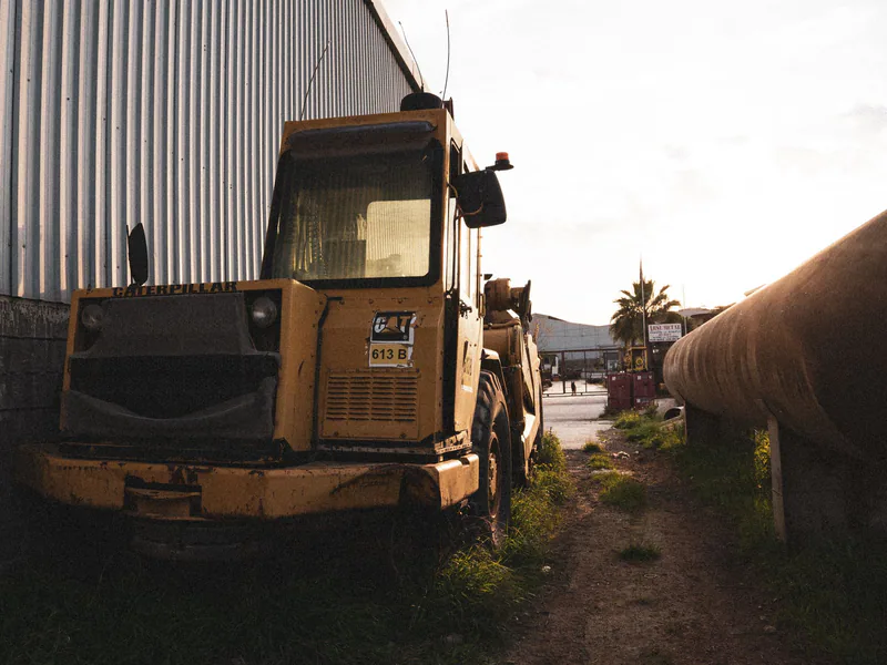 Vintage excavator parked beside a metal warehouse at sunset, exuding a moody industrial vibe