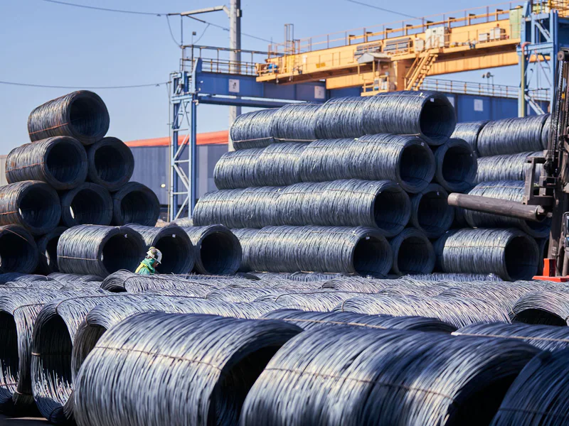 Large stacks of steel wire coils stored outdoors at an industrial site under bright daylight