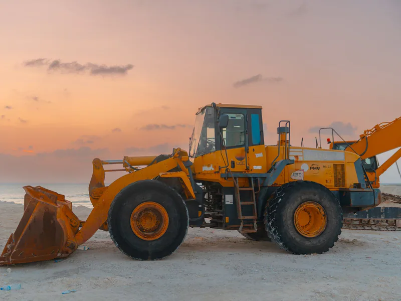 A bulldozer on a beach during sunset, ideal for projects involving coastal construction