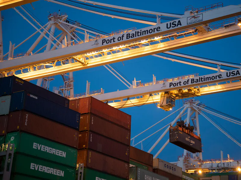 Illuminated cargo cranes at the Port of Baltimore with stacked containers at dusk