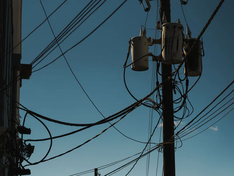 Low angle view of power lines and transformers against a clear blue sky, depicting modern electricity infrastructure