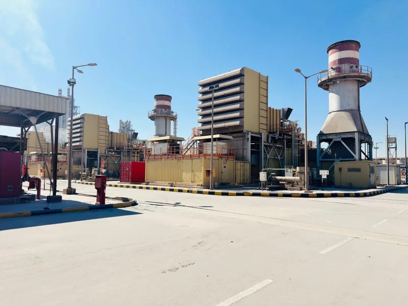 A modern power plant with turbines and chimneys under a clear blue sky in Saudi Arabia