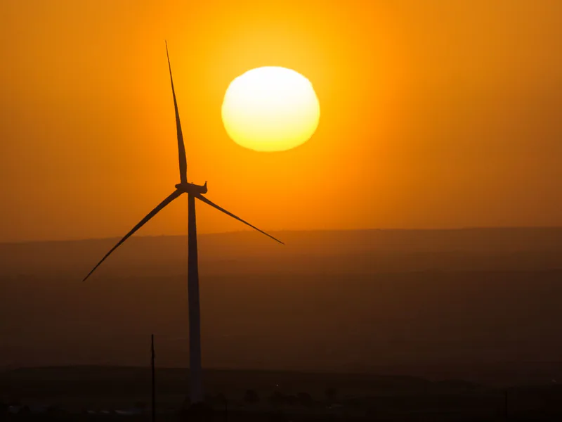 A wind turbine stands silhouetted against a vibrant sunset, symbolizing renewable energy