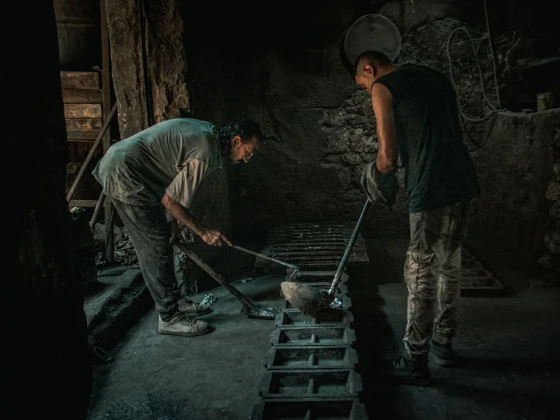Two men working with molten metal in a dimly lit foundry setting
