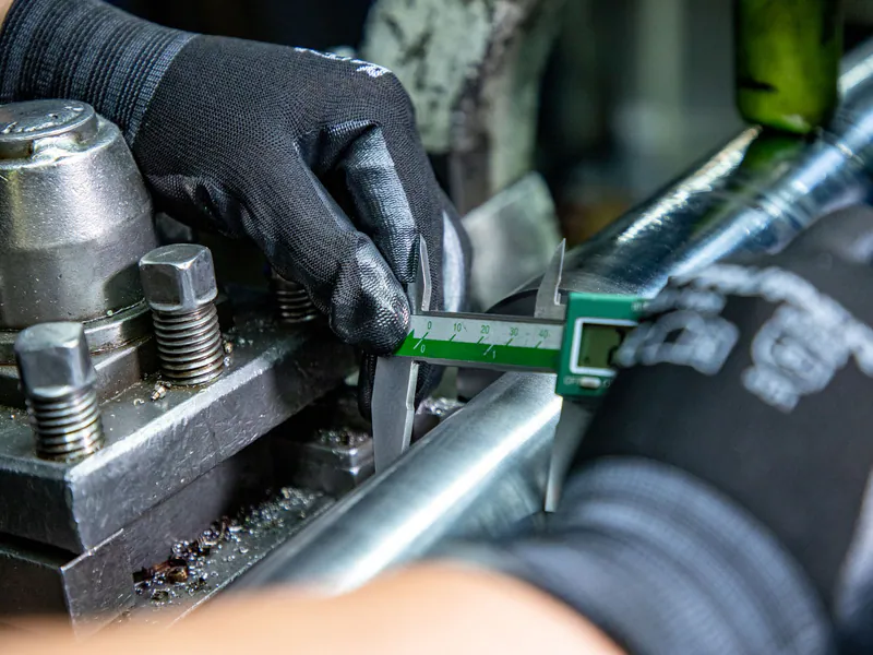 Machinist measuring a metal part with a digital caliper