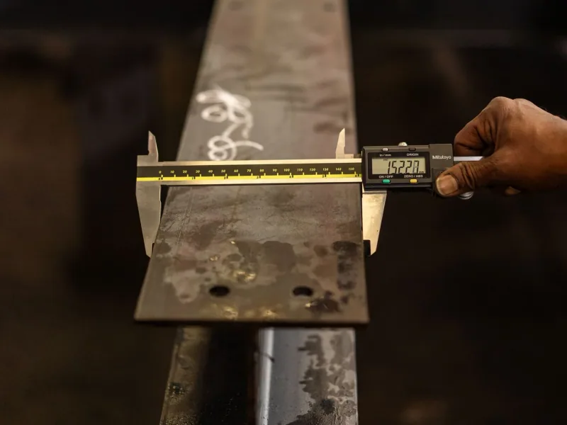 An inspector measuring the width of a cut metal bar with a digital caliper